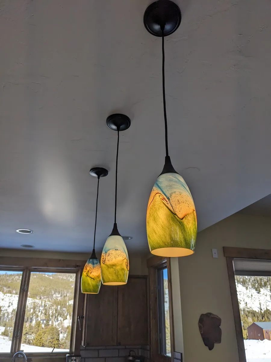 Three art-glass pendant lights hung from a kitchen ceiling by Zack, with snowy hills through the windows