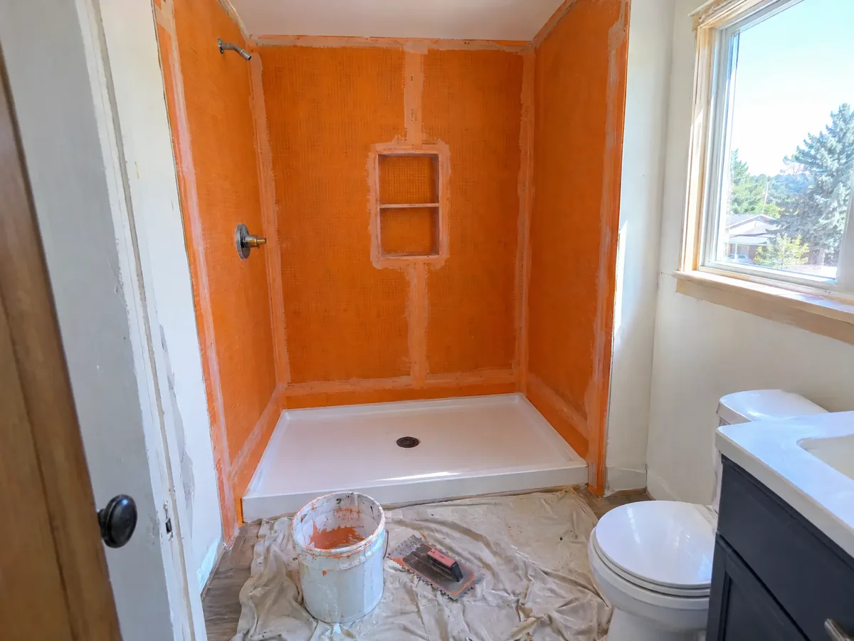 A small bathroom mid tub-to-shower conversion: a new shower pan and orange waterproofing membrane on three walls