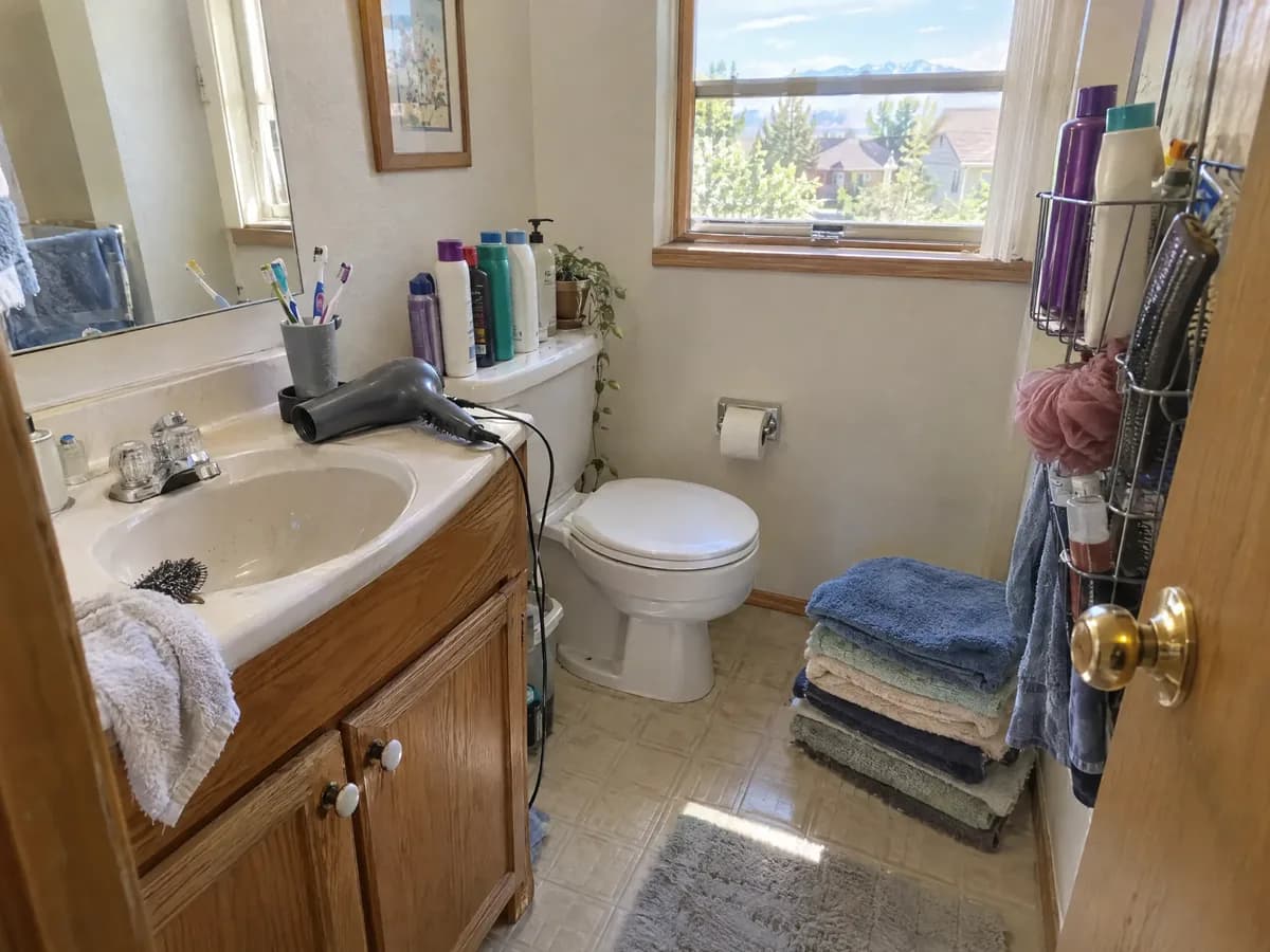 A small powder room crowded with a family's things during a remodel: four toothbrushes, bottles on the toilet tank, stacked towels
