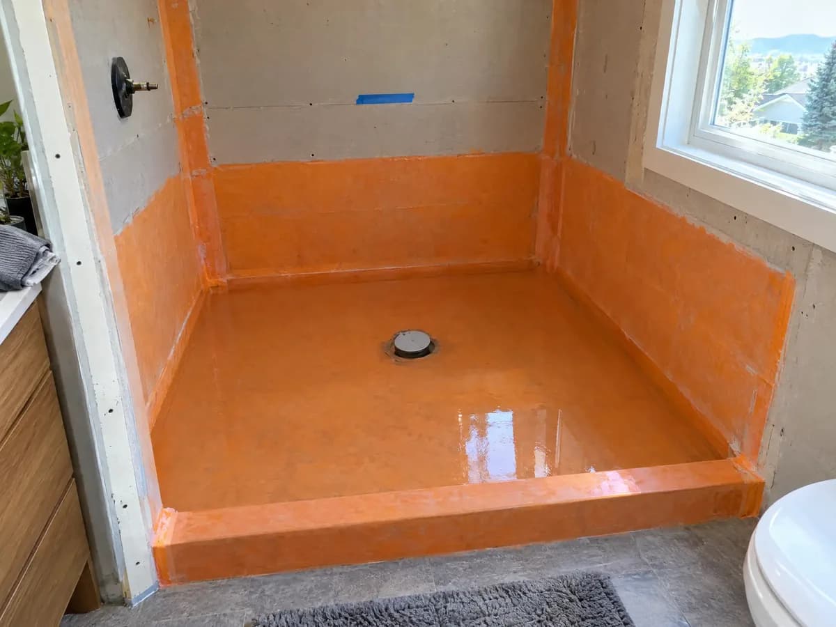 A waterproofed shower floor holding standing water for a flood test, the drain plugged, orange membrane up the walls