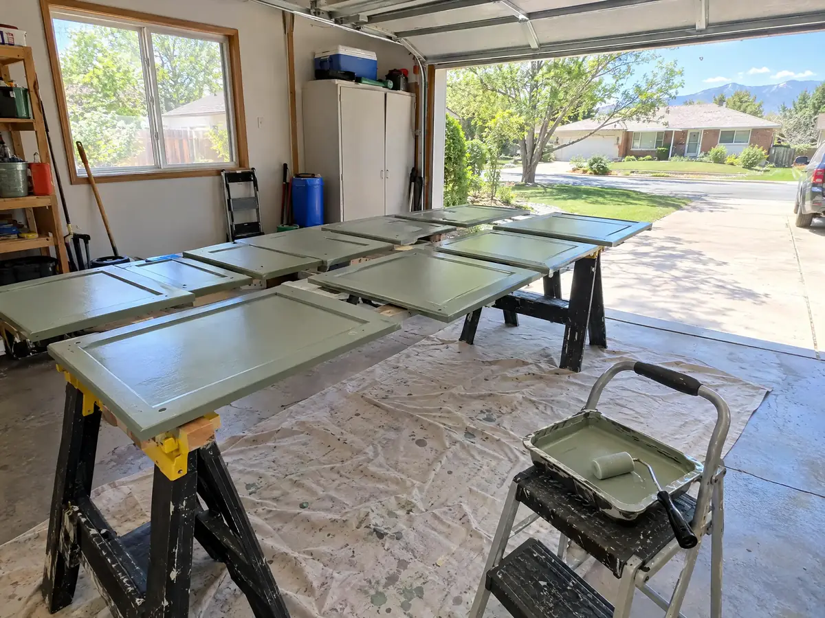 Cabinet doors painted sage green, drying on two sawhorses in a garage