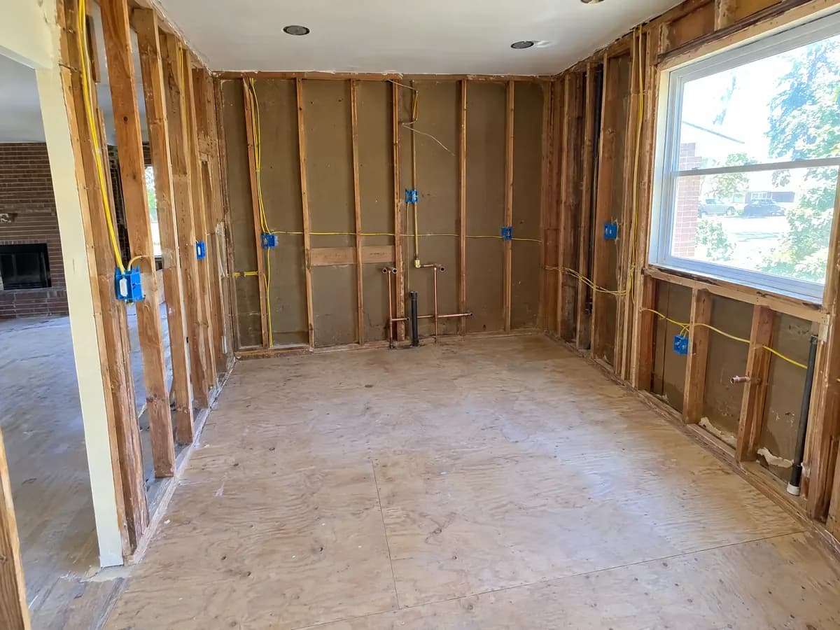 A gutted kitchen open to the studs, with copper water lines stubbed out and new blue electrical boxes on yellow cable