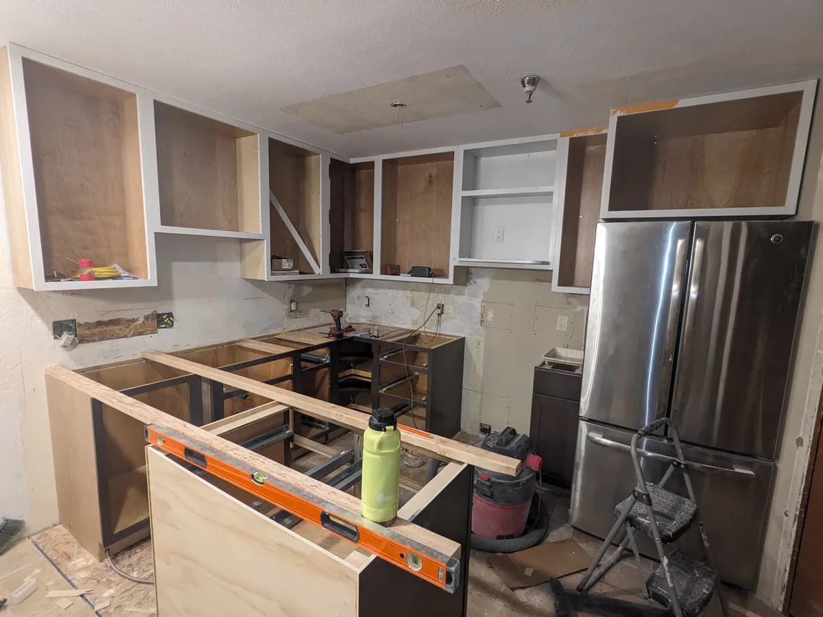 Zack's kitchen job partway through: new dark base cabinets set and leveled with no counters on, the old wall cabinet boxes still up