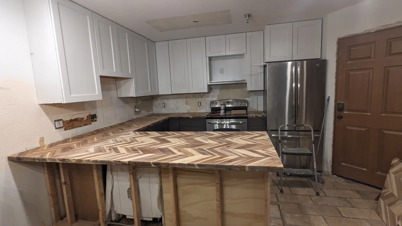 Zack's kitchen remodel partway through: white upper cabinets and dark lowers in, a chevron butcher-block counter on, the peninsula still open framing