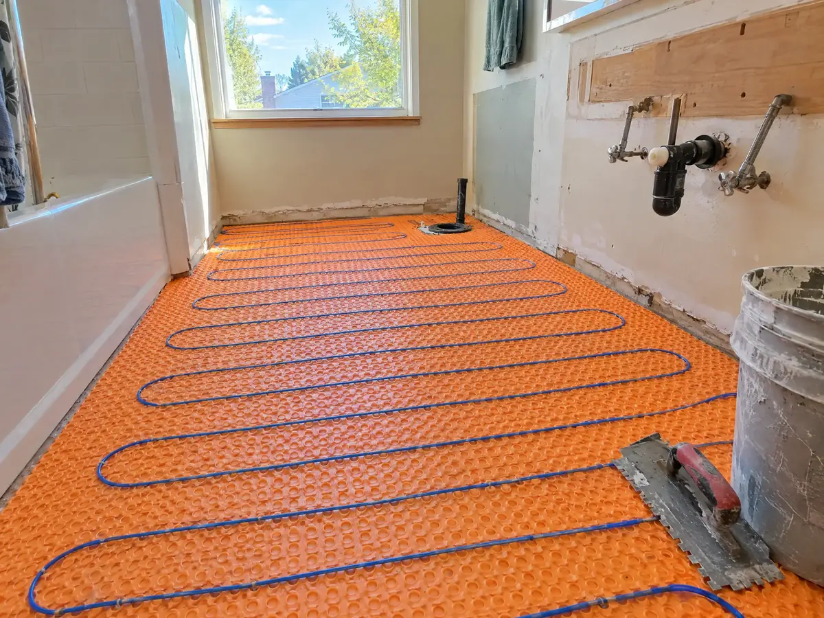 Electric floor-heating cable laid in even loops across an orange membrane on a bathroom subfloor, ready for tile