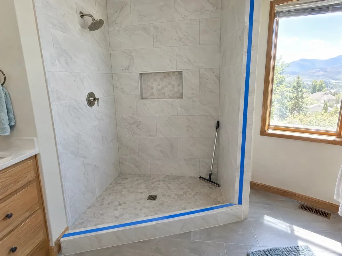 A newly tiled walk-in shower with no glass yet, blue tape marking where the glass panel will go