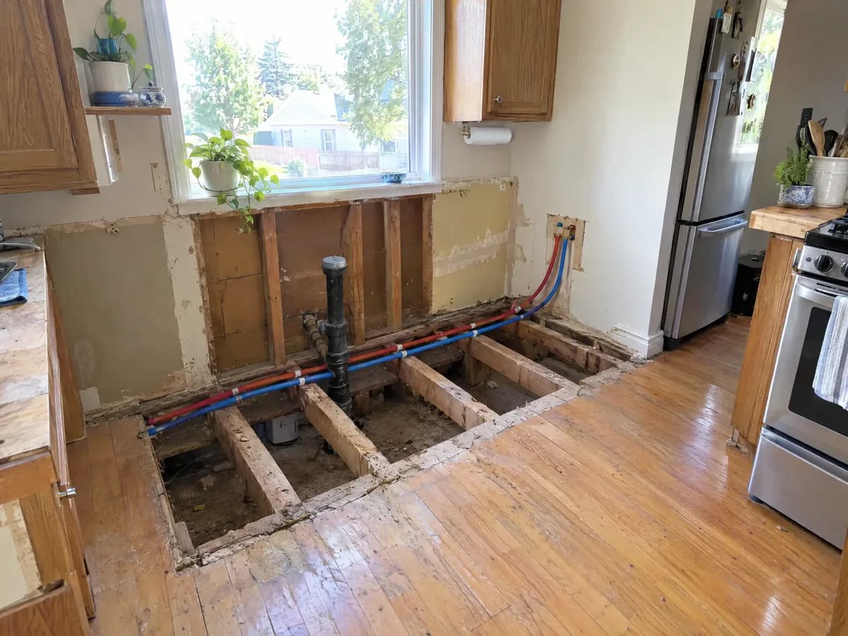 A kitchen floor opened up under the window, the old drain capped and new red and blue PEX lines running to a new sink spot