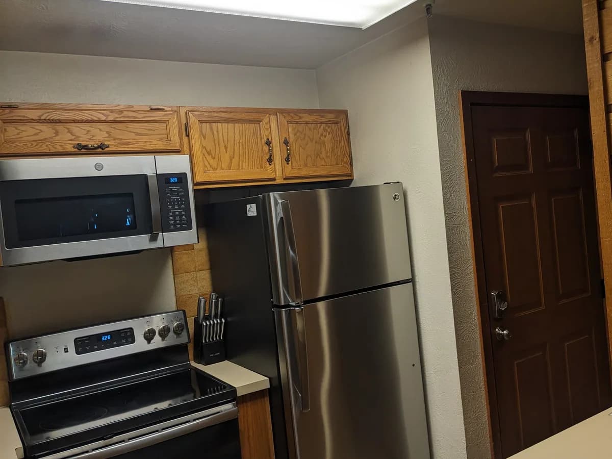 A kitchen before Zack's remodel: oak upper cabinets, a fluorescent box light, a stainless range and fridge