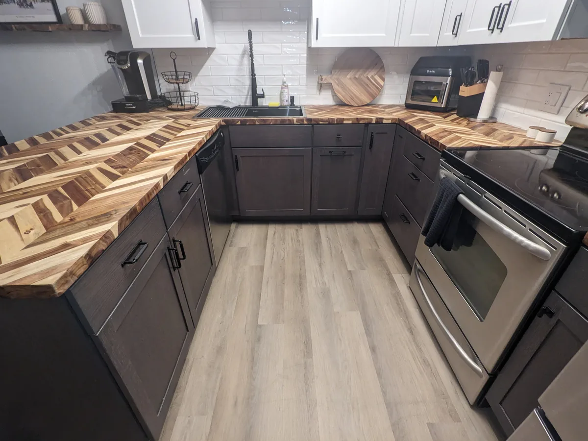 The same Golden kitchen finished: dark base cabinets, chevron butcher-block counters, a white tile backsplash and a light plank floor