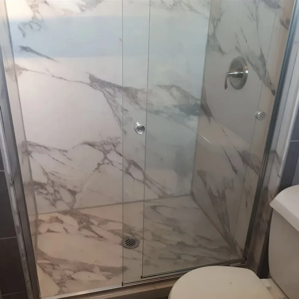 A shower Zack remodeled, with marble-look walls and floor behind a sliding glass door