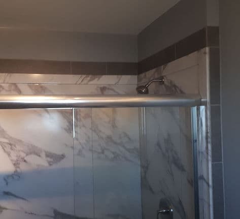 Remodeled shower with marble-look tile, a dark accent band and a sliding glass door